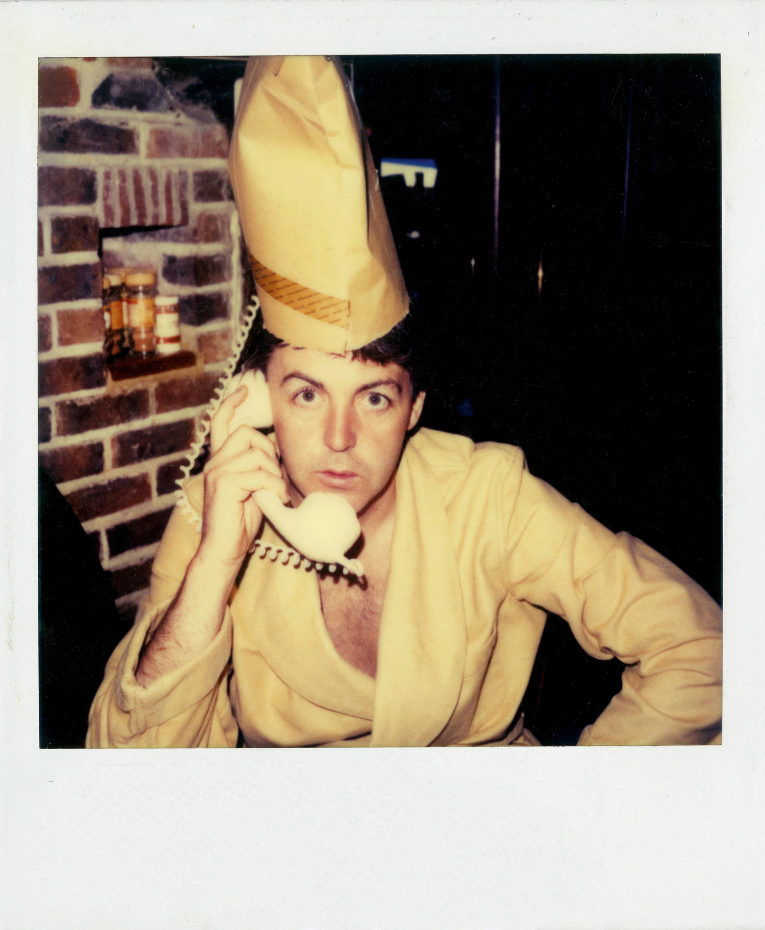 Polaroid of Paul wearing yellow dressing gown on the phone with envelope on head